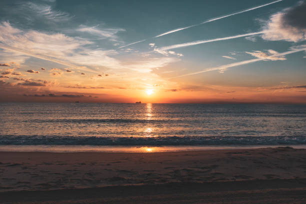 istock Beach landscape with sun falling at sunset and boat on sea line 1413636685