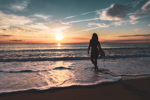 Silhouette of woman on beach with surfboard at sunset