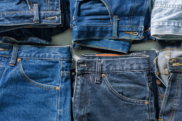 vue de dessus de jeans pliés, jeans bleus sur une pile de jeans. vue de dessus de divers tissus en denim sur fond blanc. plusieurs jeans longs - vibrant color empty stack heap photos et images de collection