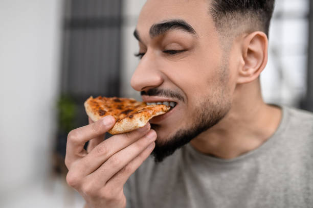istock Face of man biting pizza sideways to camera 1413639640