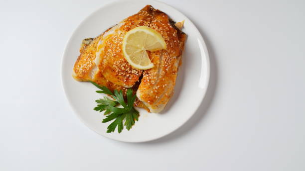 istock Fresh backed tilapia fillet on white plate with lemon and herbs 1413640921