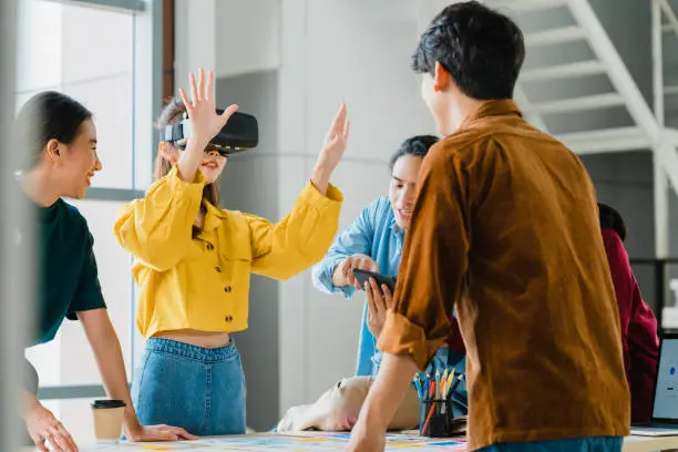 Asian businessmen and businesswomen meeting brainstorming ideas using vr glasses (virtual reality) testing mobile app from develop software working together in modern office. Coworker teamwork concept