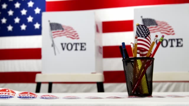A slider shot along a table from a pencil cup to “I VOTED TODAY!” stickers with voting booths and large America flag