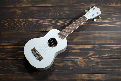 White colored wooden ukulele guitar on the brown wooden background. Hawaiian Four String Guitar. Musical Instrument.