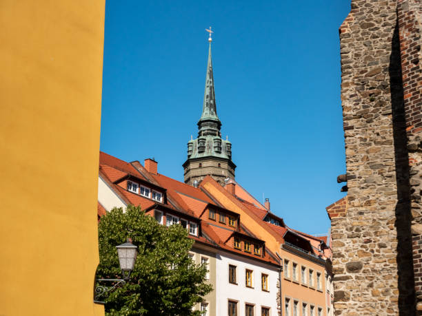 The church tower in Bautzen, Germany is behind small buildings in the town. Beautiful ensemble of architecture in Saxony. Facades of a row of small houses in good condition. Landmark in the city.