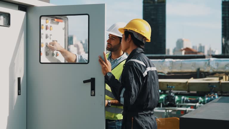 Male engineer and worker inspecting electrical control panel.