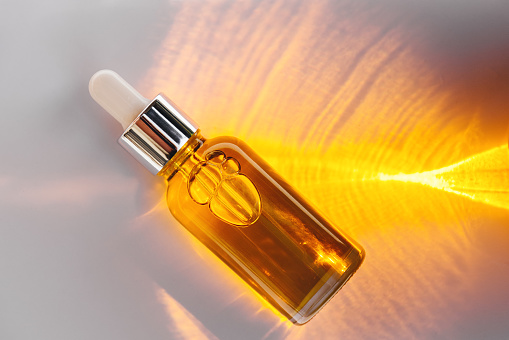 Mockup of glass dropper bottle with a metal cap and yellow essential oil on a background with an abstract fire pattern of light and shadow. Eco cream, serum, cosmetics, massage oil. Copy space