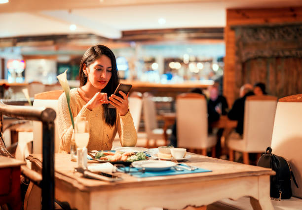 istock latin young woman sitting alone in a restaurant using smartphone 1413647032