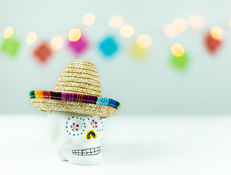 Skull decorated with Mexican hat on white background with out of focus lights. Day of the dead in Mexico. Copy space.