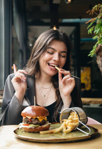 Attractive young woman eating french fries and a burger in a restaurant. stock photo
