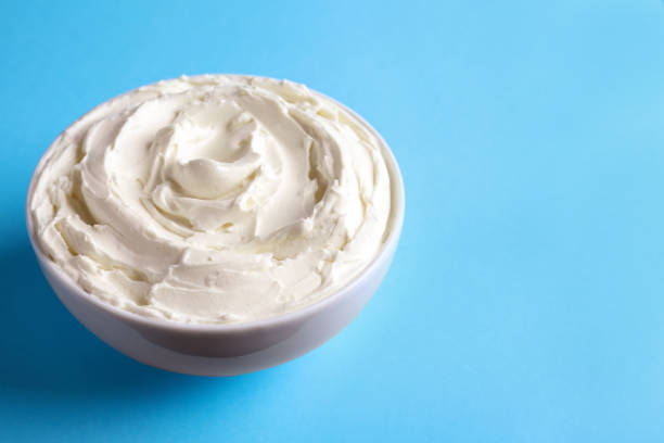 istock Bowl of tasty cream cheese on light blue background, space for text 1413648439