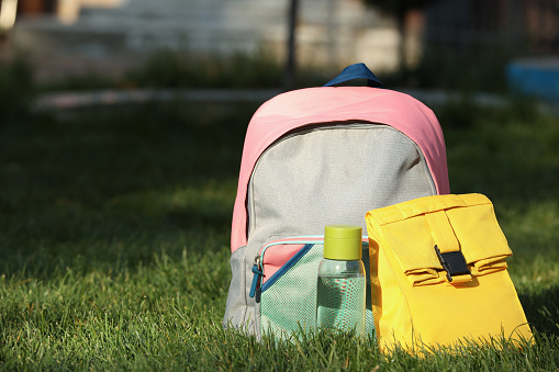 Backpack, lunch bag and bottle of water on green grass outdoors, space for text