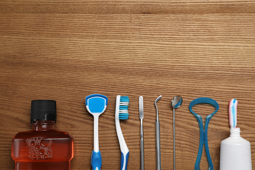 Flat lay composition with tongue cleaners, dentist instruments and teeth care products on wooden table, space for text
