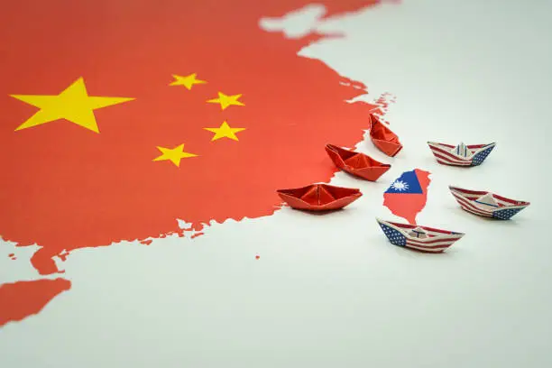Paper boats with the colors of the USA and China surrounding the island of taiwan on a map. China and taiwan war and conflict concept.