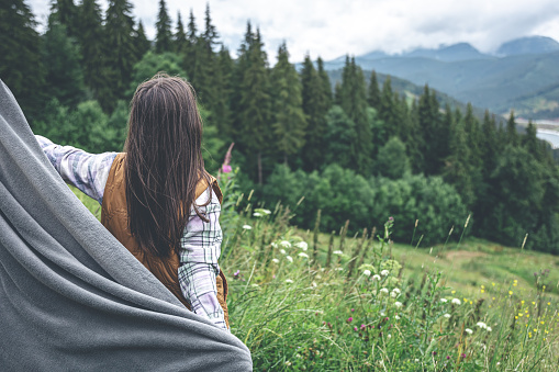 A young woman wrapped in a plaid in the mountains on a blurred background, copy space.