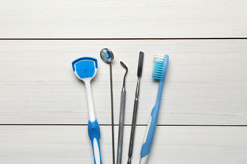 Tongue cleaner, dental instruments and toothbrush on white wooden table, flat lay