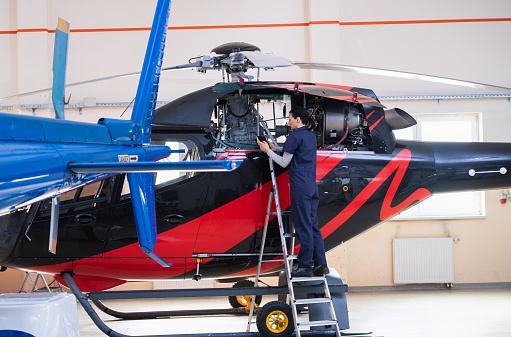 Female aero engineer in uniform standing on ladder near jet, with digital tablet, working and checking helicopter. Safety and aviation concept.