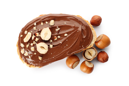 Bread with tasty chocolate spread and pieces of hazelnuts on white background, top view