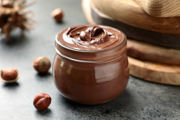 istock Glass jar with tasty chocolate hazelnut spread and nuts on grey table 1413653627