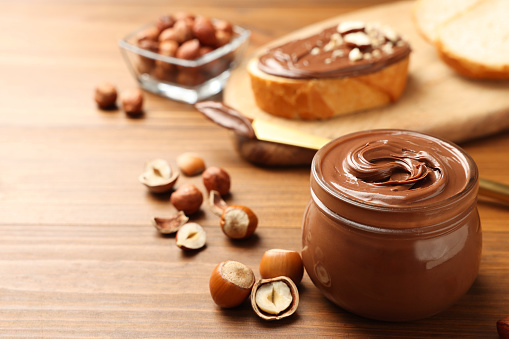 Glass jar with tasty chocolate hazelnut spread and nuts on wooden table. Space for text