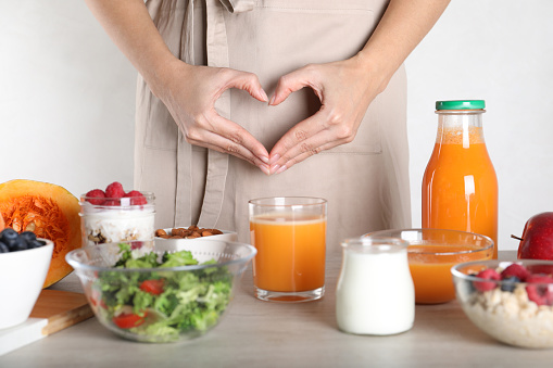 Woman making heart near table with food, closeup. Balanced nutrition for healthy digestive system