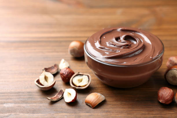 istock Glass bowl with tasty chocolate hazelnut spread and nuts on wooden table. Space for text 1413654579