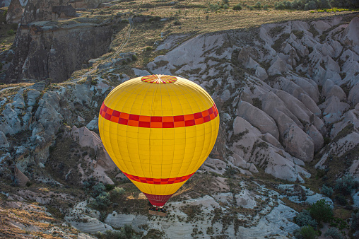 A yellow hot air balloon carrying tourists passes over rock formations in Goreme