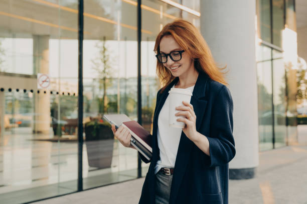 istock Smiling redhead woman corporate worker dressed in formal clothes drinks coffee 1413658638