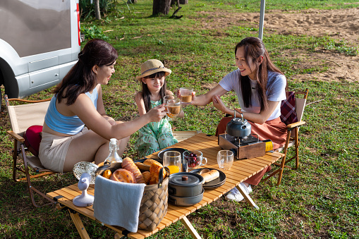 Two Asian women and a little girl travelling on holiday vacation with camper van enjoy picnic and breakfast at the beach in early morning.