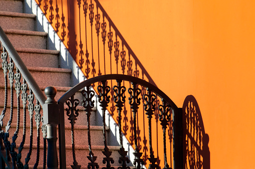 Close up view of staircase, cast iron handrail  fence, gate and shadow, orange painted wall. Copy space on the right.