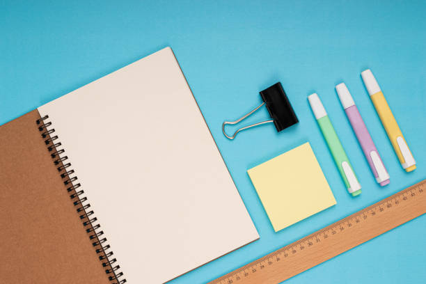 Notebook, colored pencils, ruler, note paper and clamp. back to school. Isolated blue background