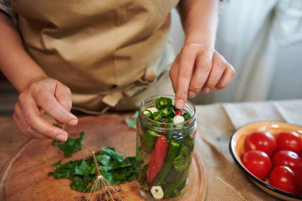 istock Cropped view of housewife's hand adding fragrant culinary herbs in freshly marinated chili peppers. Close-up pickling 1413659766