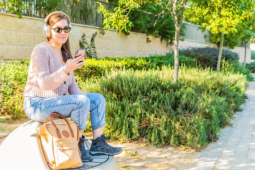 Woman watching videos in a smart phone with headphones sitting in a park.