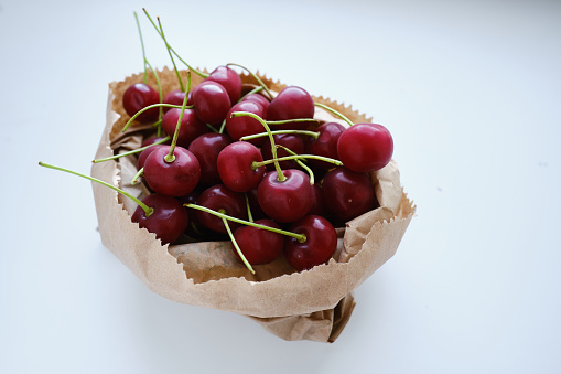 Delicious ripe cherries in a craft bag on a light background. The concept of proper nutrition, diet and lifestyle. Juicy berry close-up. Vegetable food. Fresh vitamins. Organic eco product, farm