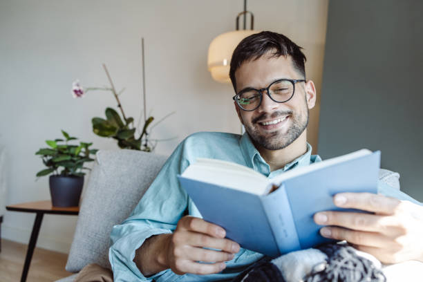 istock Smiling man reading a book while relaxing on the sofa. 1413662218