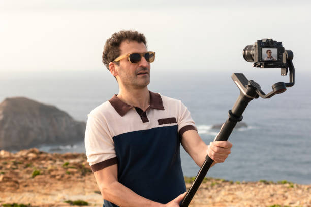 istock Gimbal for film production with 3-axis stabilizer for digital dsrl cameras or mirrorless cameras or mobile phones. Man with gimbal and monkey standing recording stabilized shots outdoors 1413662263