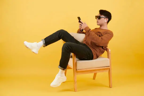 Serious young man sitting on armchair and texting friends