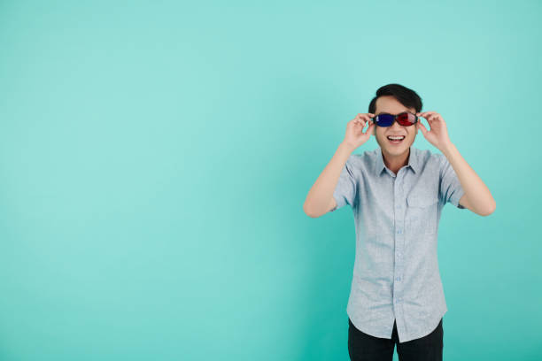 Happy excited young man wearing red and blue glasses when standing against turquoise background