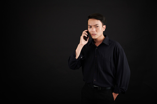 Sad stressed young man in black clothes talking on phone