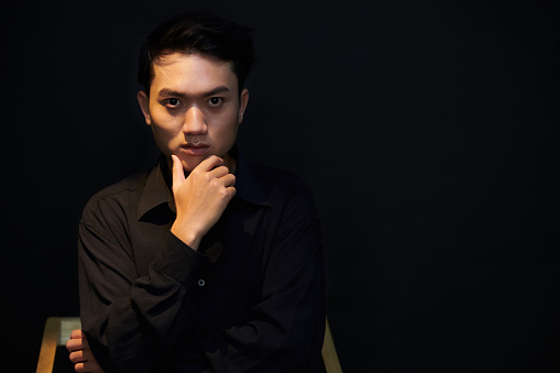 Portrait of confident serious young man touching his chin and looking at camera