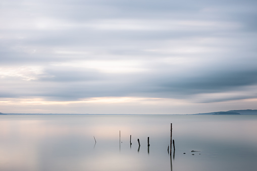 Long exposure view of fishing net poles on a lake, with perfectly still water and moving clouds.