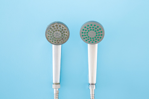 New and old shower heads on light blue table background. Pastel color. Compare two objects with and without limescale. Dirty and clean. Closeup. Top down view.