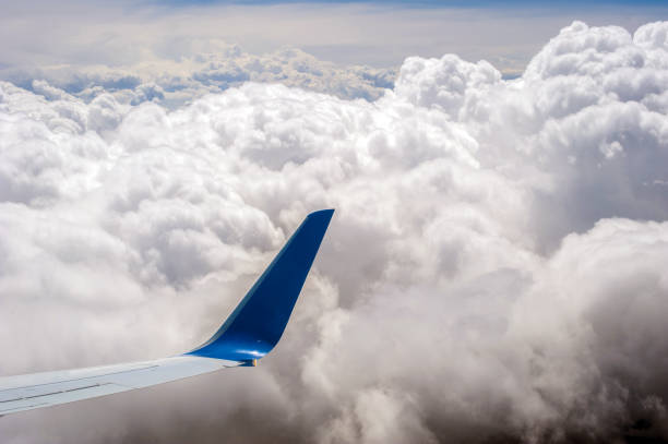 Window view of wing of airplane advancing through clouds
