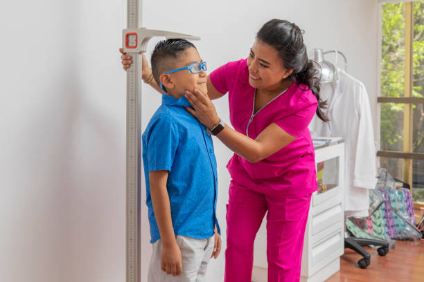 Pediatric female doctor holding a child's head while measuring it with a floor ruler Pediatric female doctor holding a child's head while measuring it with a floor ruler. boy height measure stock pictures, royalty-free photos & images
