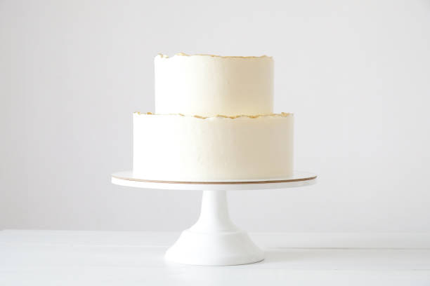 istock Cake with white cream, decorated with gold confectionery sprinkles on a white background. Two-tiered white wedding cake. 1413671973