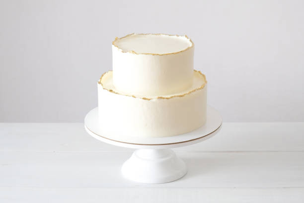 istock Cake with white cream, decorated with gold confectionery sprinkles on a white background. Two-tiered white wedding cake. 1413672001