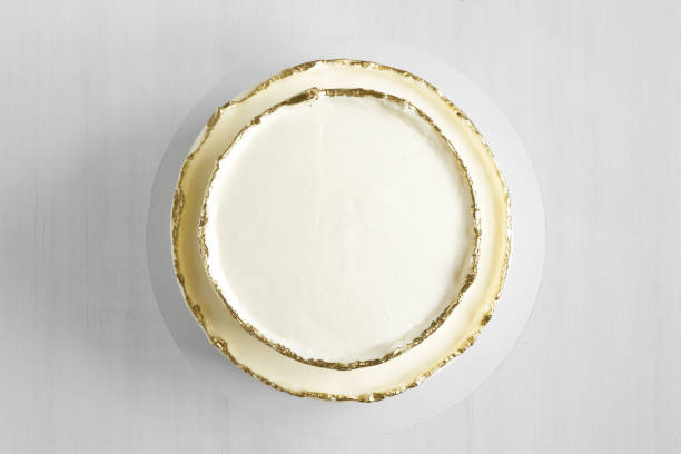 istock Cake with white cream, decorated with gold confectionery sprinkles on a white background. Two-tiered white wedding cake. Top view. 1413672005