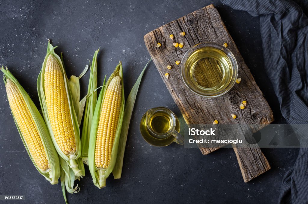 Corn oil in glass bowl with fresh ripe corn cobs on rustic table, cooking oil composition Corn Maze Stock Photo