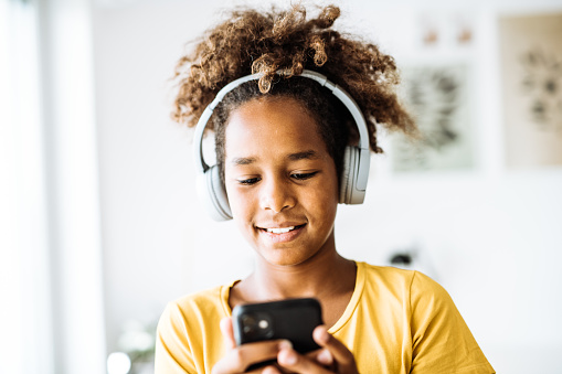 African American girl relaxing on mobile phone or laptop, listening to music or playing games