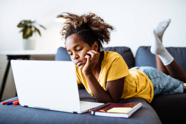 Eleven year old African-American school girl doing homework at home on laptop, expressing sadness or boredom stock photo